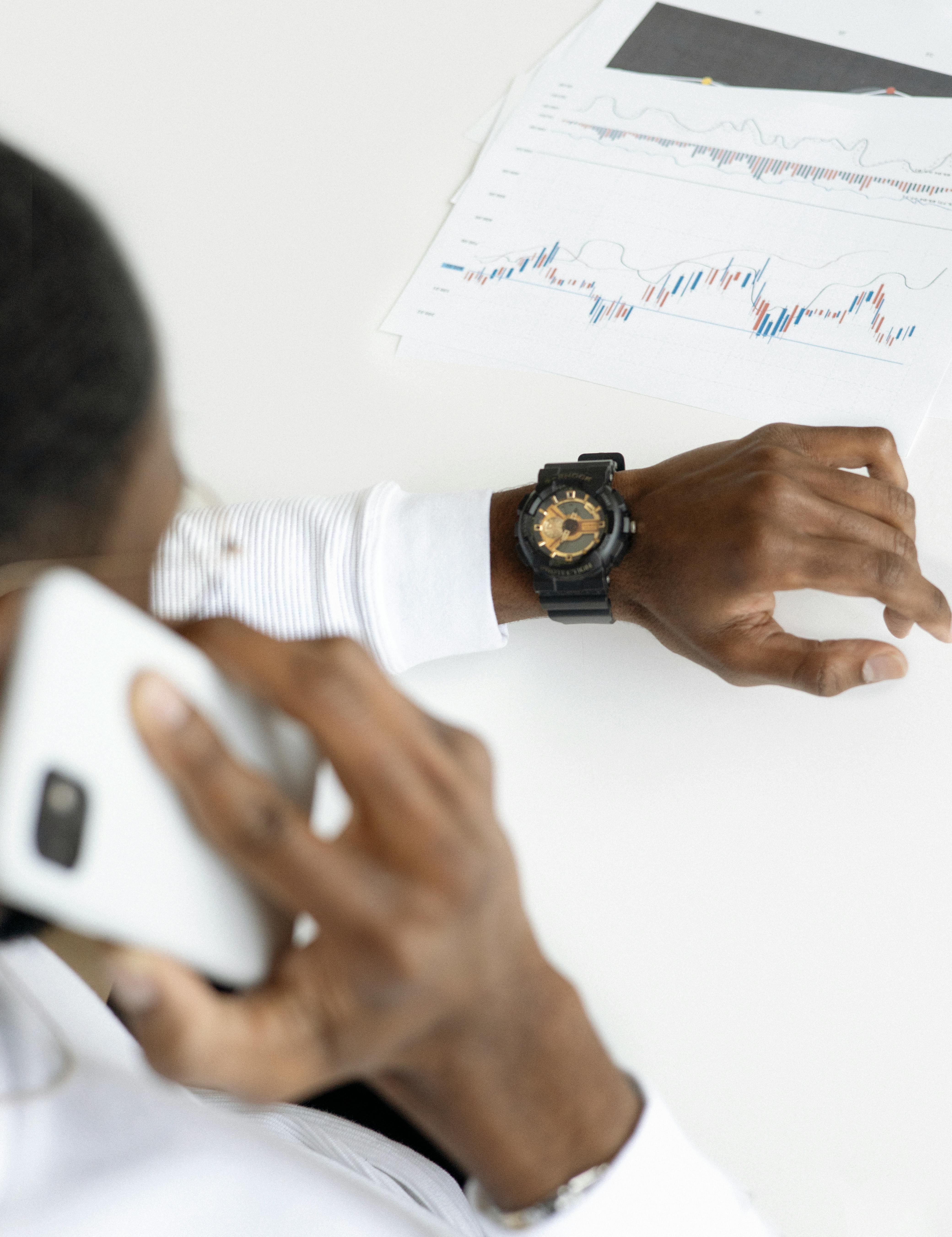 man talking on the phone, while glancing at his watch, financial reports are in front of him on the table